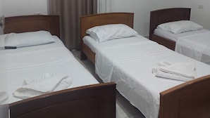 A hotel room with three single beds, each with a wooden headboard, white linens, and a white towel on the bed. - Casa Mia Hostel SR (Sarandë)