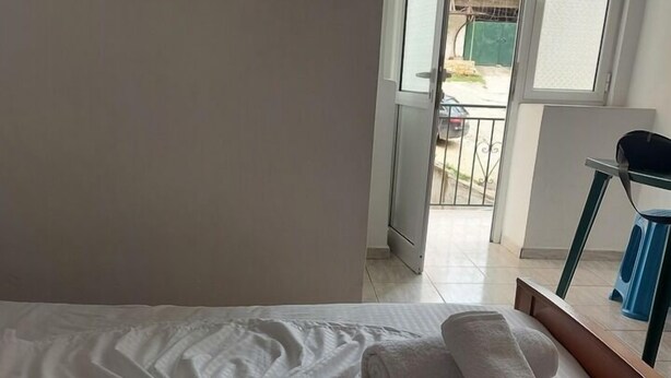 A hotel room with a neatly made bed, a chair, and a view of the outside balcony. - Casa Mia Hostel SR (Sarandë)
