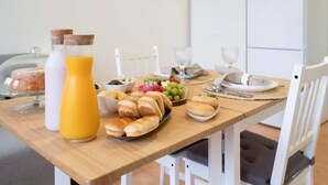 Een ontbijttafel met brood, gebak, fruit en flesjes sap.