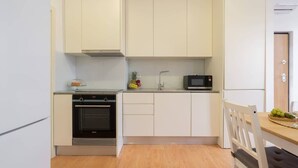 Een compact keukenblok met witte kastjes, een magnetron, een fornuis en een klein aanrecht met fruit.