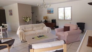A living room with a sofa, armchairs, a coffee table, and a dining area with chairs. - LA Rocanya Villa Classée 4 Avec Chambres Climatisées Piscine Privée Sécurisée (Laroque-des-Albères)