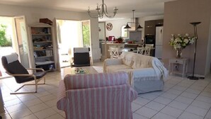 A spacious living room with a sofa, armchair, and a television. There is a kitchen area in the background with a dining table and chairs. - LA Rocanya Villa Classée 4 Avec Chambres Climatisées Piscine Privée Sécurisée (Laroque-des-Albères)
