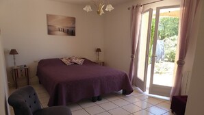 A bedroom with a bed, two bedside tables, a chair, a chandelier, and a door leading to a balcony. - LA Rocanya Villa Classée 4 Avec Chambres Climatisées Piscine Privée Sécurisée (Laroque-des-Albères)