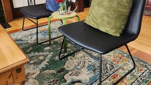 A living room with two black chairs, a green cushion, a patterned rug, a small table with a vase of flowers, and a lamp. - Historic Craftsman 3 Bedroom Home in Uptown Butte (Butte)