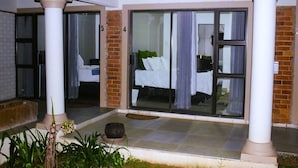 Habitación de hotel con un gran ventanal corredero, una cama con ropa blanca y un pequeño balcón con plantas.