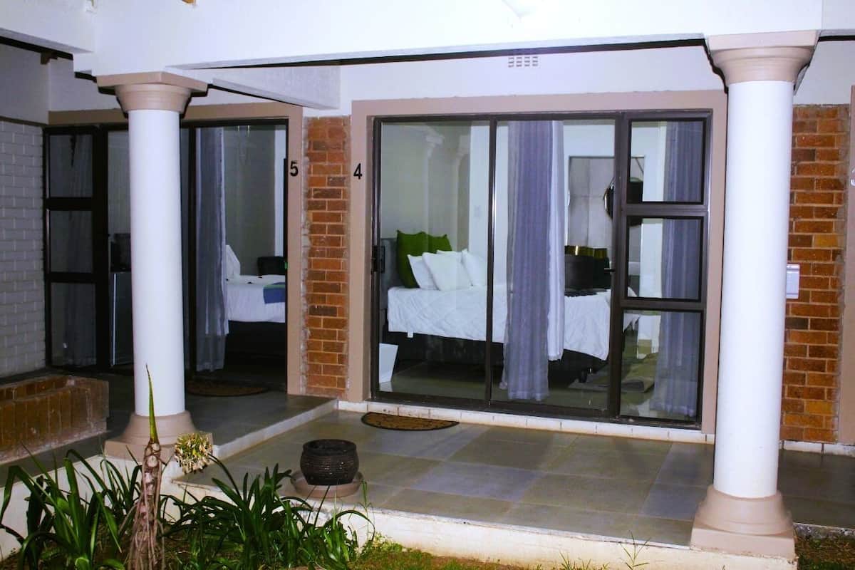 A hotel room with a large sliding glass door, a bed with white linens, and a small balcony area with plants.