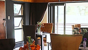 Un comedor con una mesa dispuesta para dos personas, sillas, un jarrón con flores y vistas a través de un ventanal.
