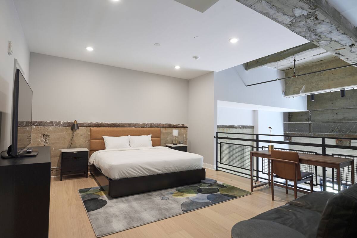 A modern bedroom with a bed, bedside tables, a desk, and a balcony with a railing.