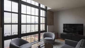 Una sala de estar moderna con ventanas amplias, un televisor de pantalla plana y dos sillones.