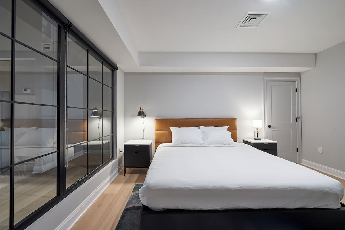 A modern bedroom with a large bed, a nightstand, a lamp, and a sliding glass door leading to a balcony.