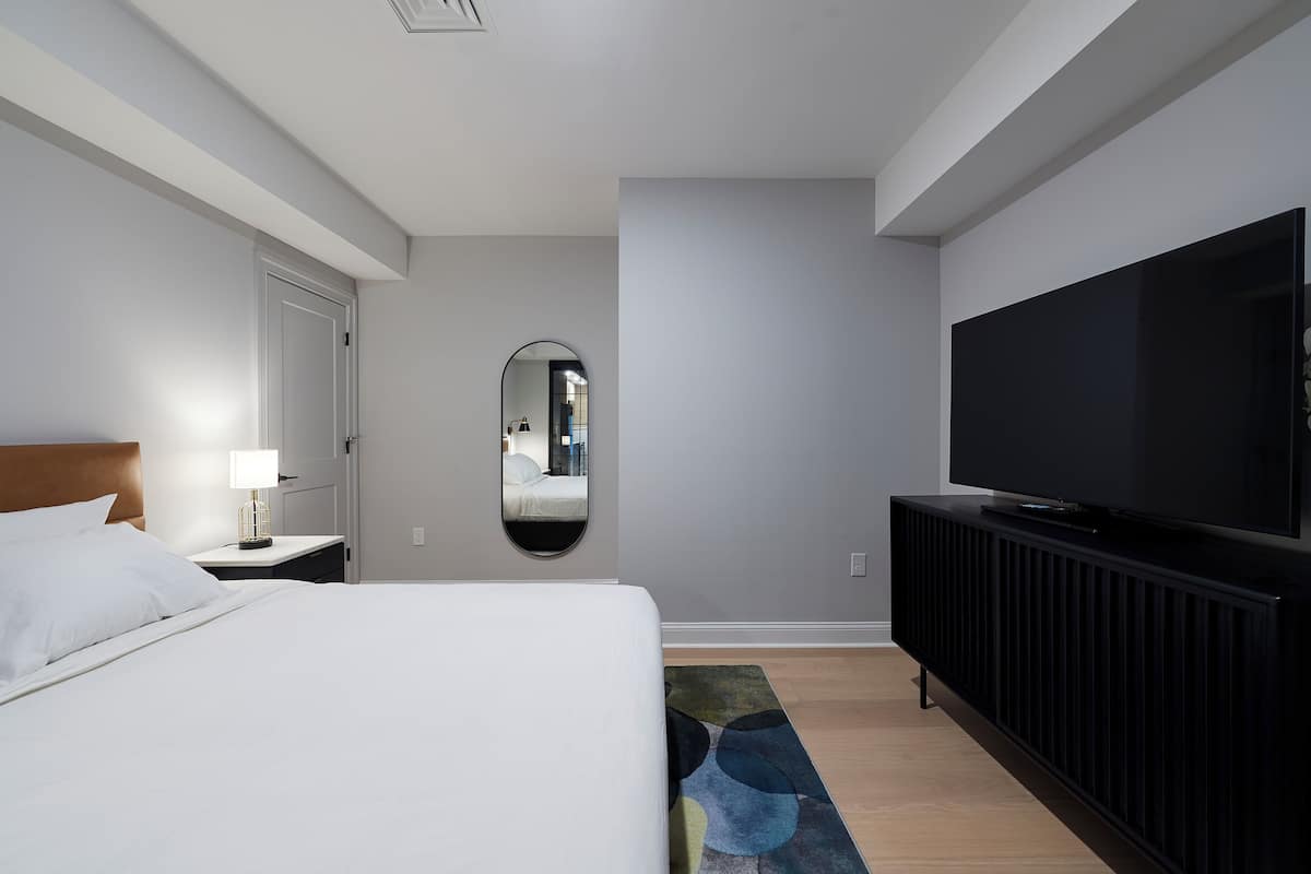 A hotel room with a bed, a TV, a mirror, and a nightstand.
