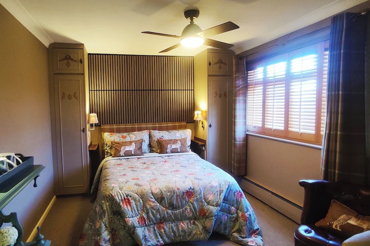 Een slaapkamer met een bed, een kaptafel met spiegel, een bureau en een plafondventilator.