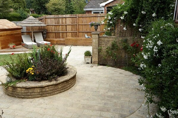 Un jardin avec une terrasse en pierre, une clôture en bois et un espace aménagé avec des plantes et des fleurs.