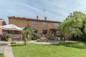Una casa de ladrillo de dos pisos con un jardín delantero, un patio y un paraguas grande.