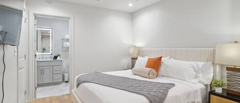 A modern bedroom with a bed, bedside tables, a ceiling fan, and a bathroom visible through an open door.