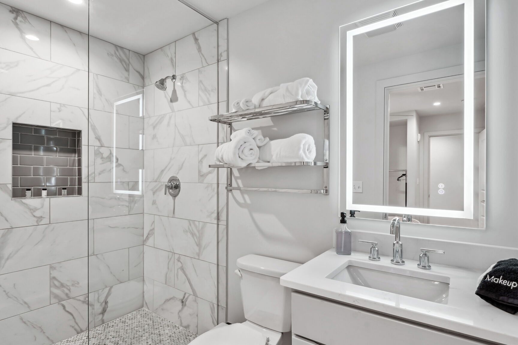 Une salle de bain moderne avec une douche à parois de verre, des toilettes, un lavabo avec un miroir et un espace pour ranger les serviettes.