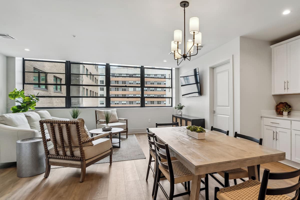 Une cuisine moderne avec des meubles blancs, une table à manger en bois et un lustre.