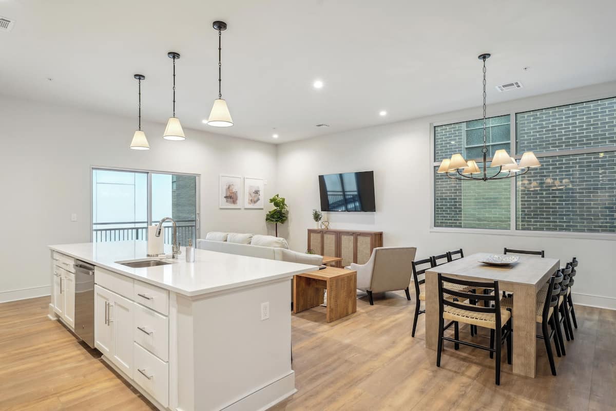 Une cuisine moderne dotée d’un îlot central, de meubles blancs et de luminaires suspendus.
