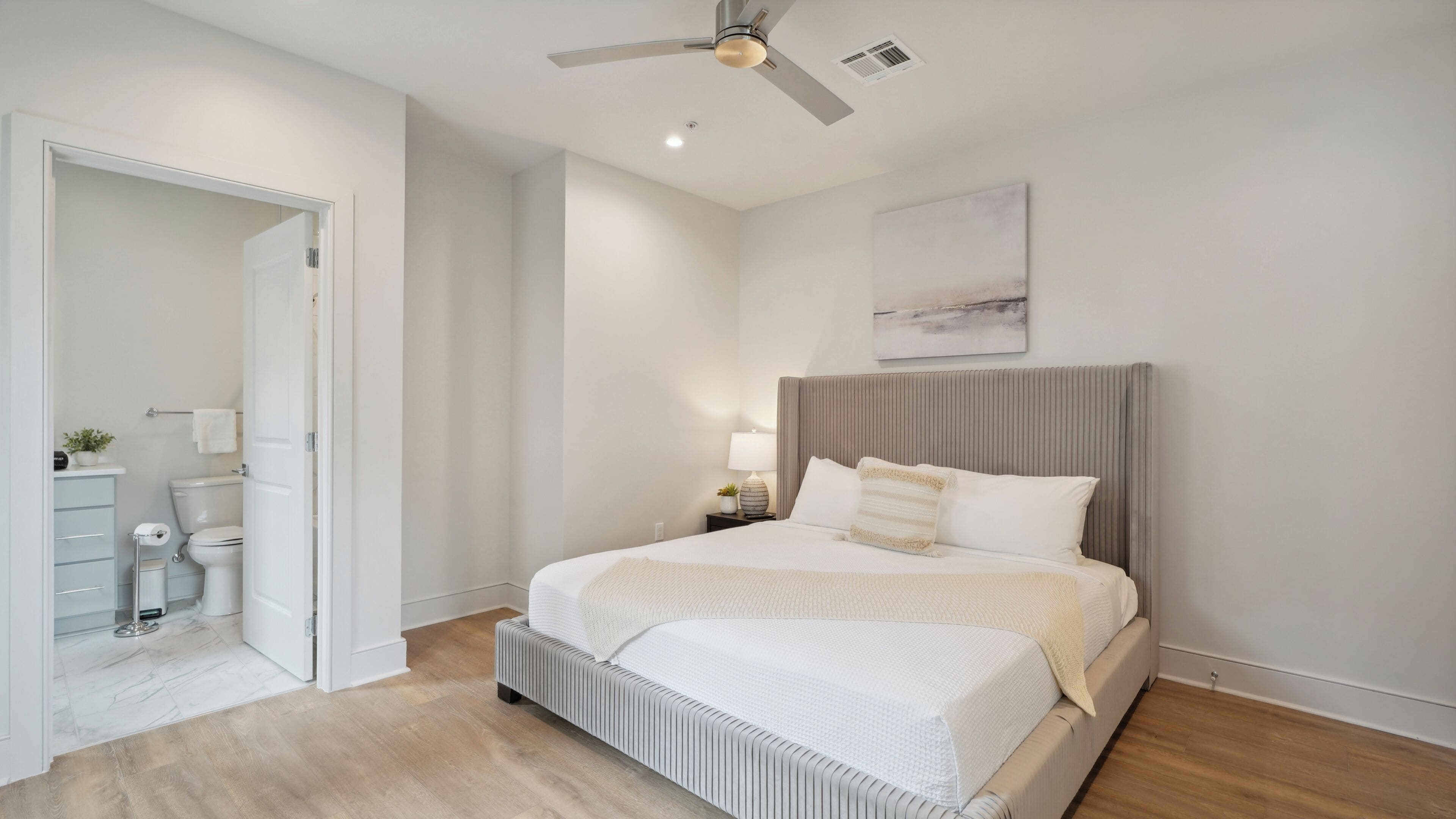 A modern bedroom with a large bed, a ceiling fan, and a view of the bathroom.