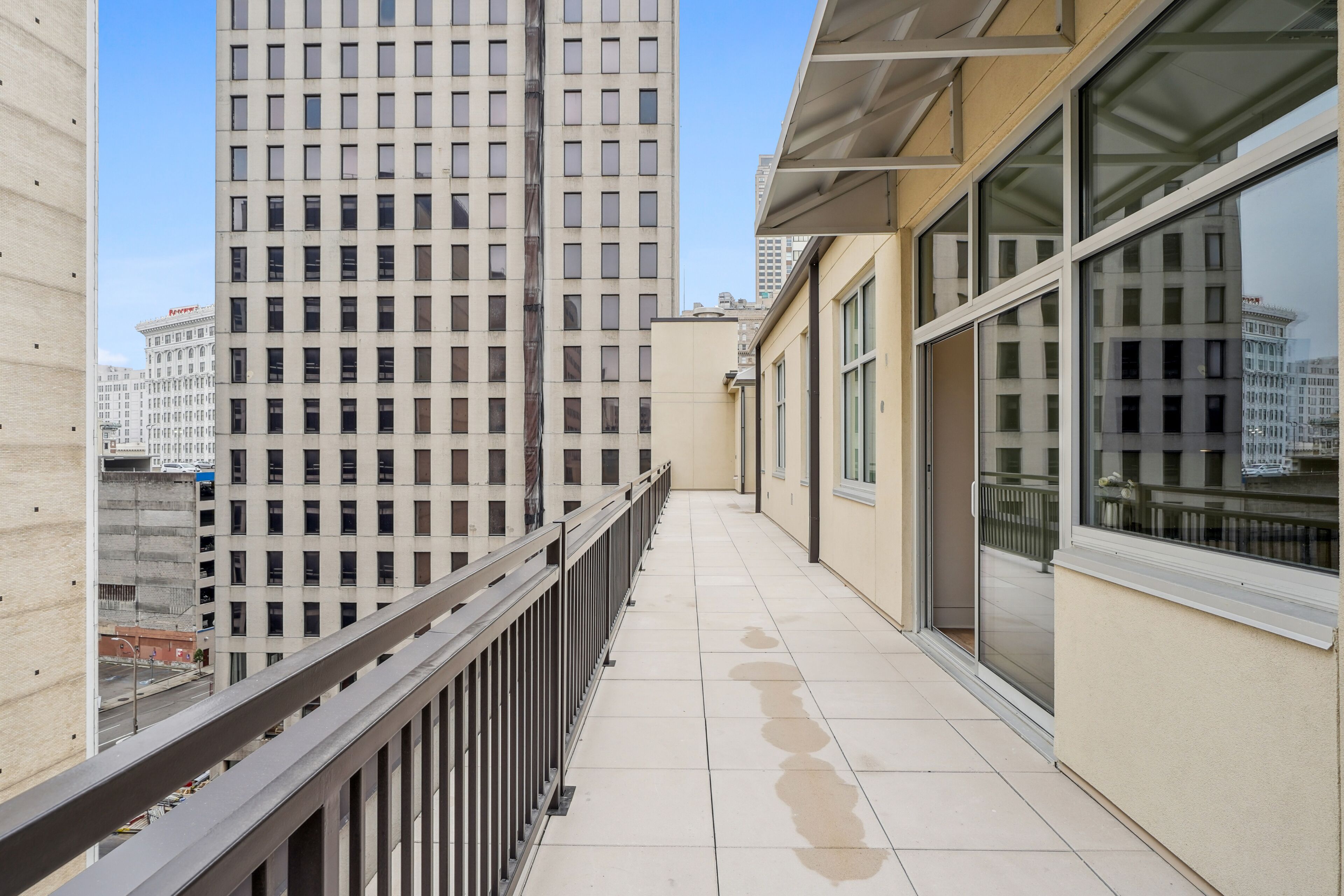 A balcony with a view of tall buildings, a tiled floor, and a metal railing.