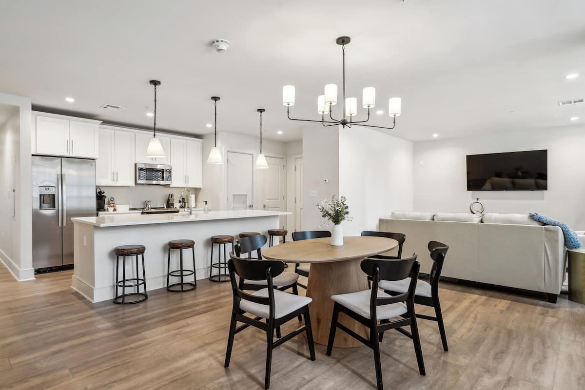 Une cuisine moderne avec des meubles blancs, un îlot central doté de tabourets et un coin repas avec une table et des chaises en bois.