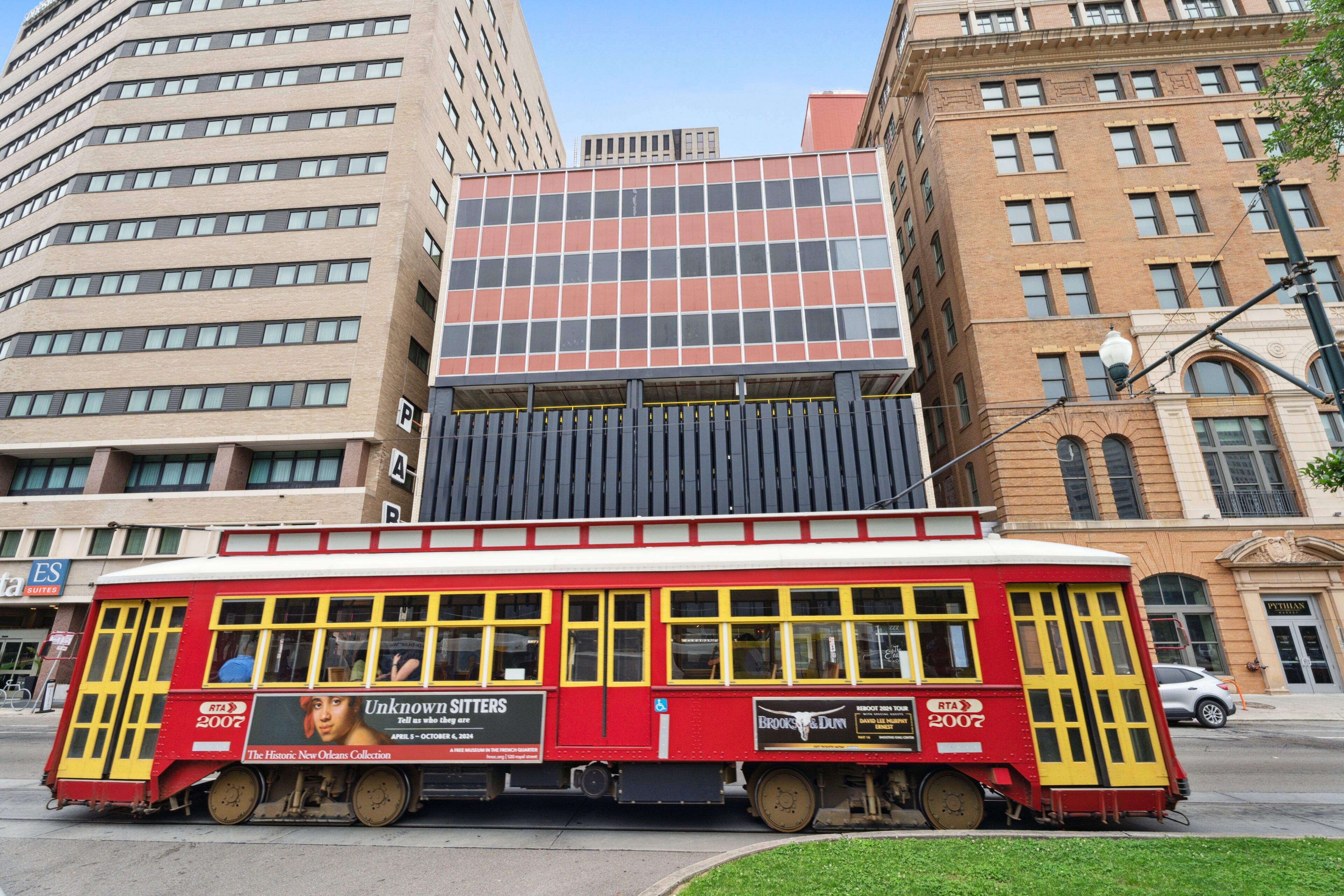 Un tranvía rojo con publicidad que pasa por un edificio moderno con grandes ventanales.