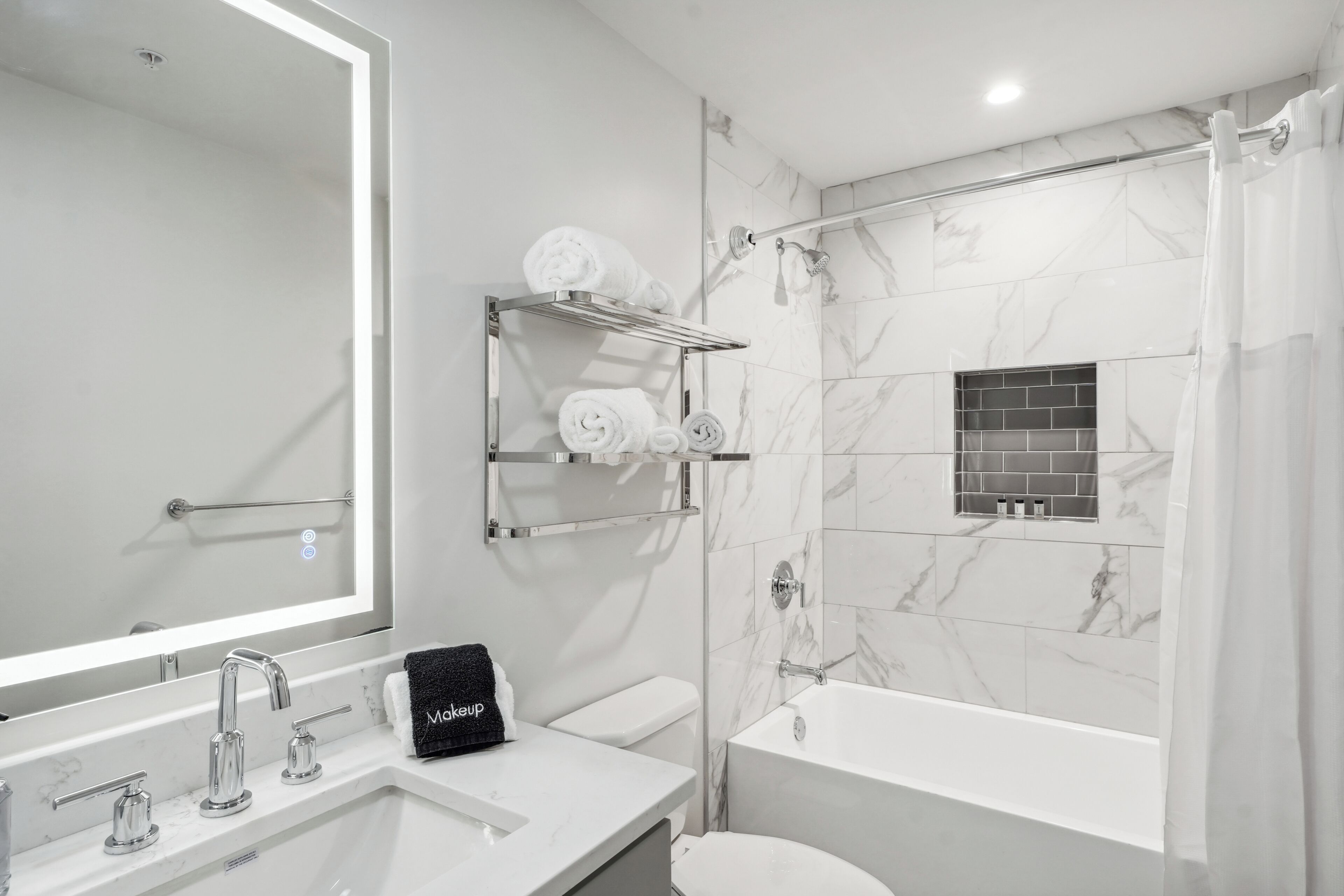 Een moderne badkamer met een grote spiegel, een wastafel met drie kraan, een toilet, een badkuip en een douche met gordijn.