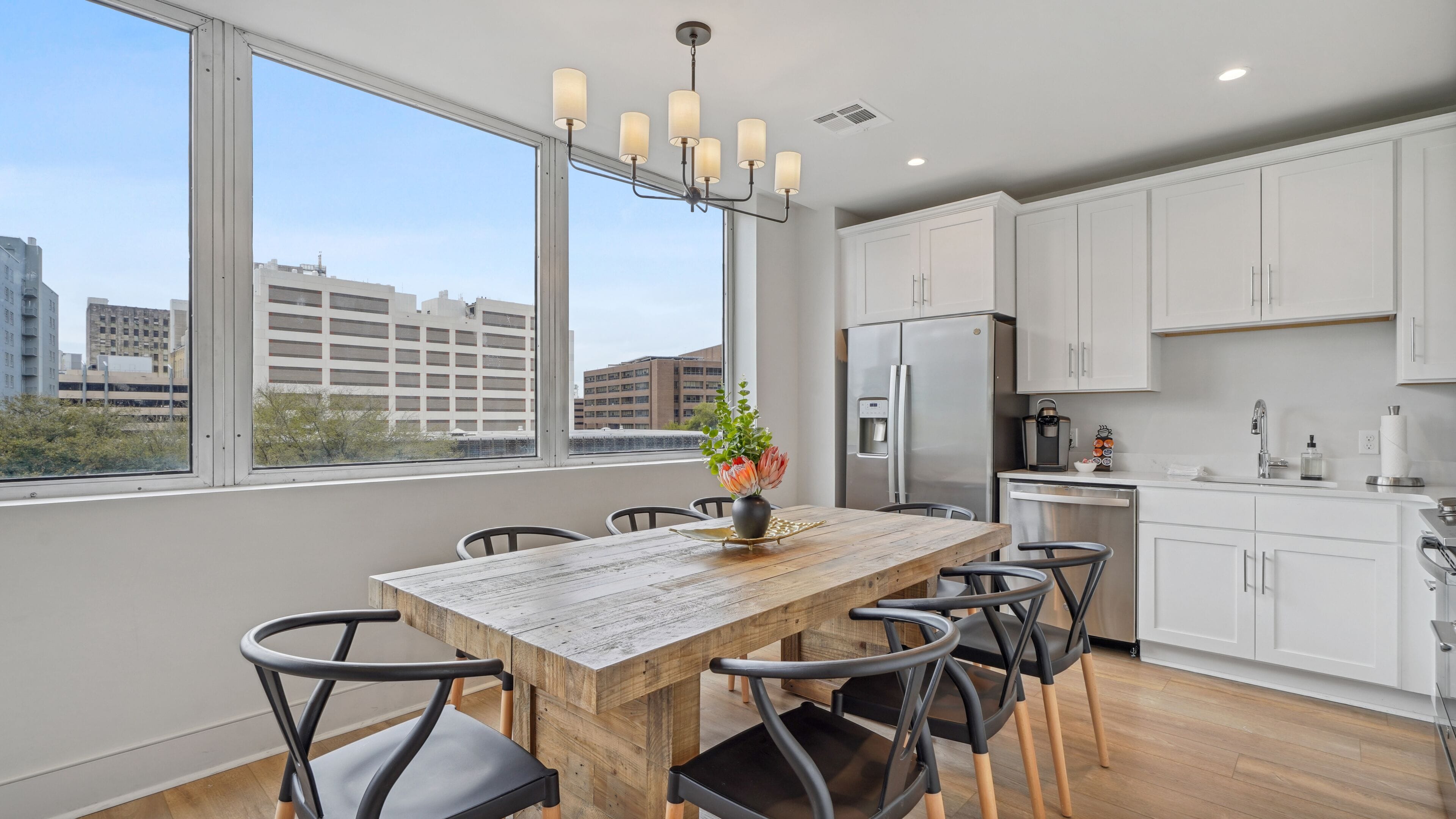 A modern kitchen with white cabinets, a stainless steel refrigerator, and a wooden dining table with chairs.