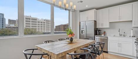 A modern kitchen with white cabinets, a stainless steel refrigerator, and a wooden dining table with chairs.