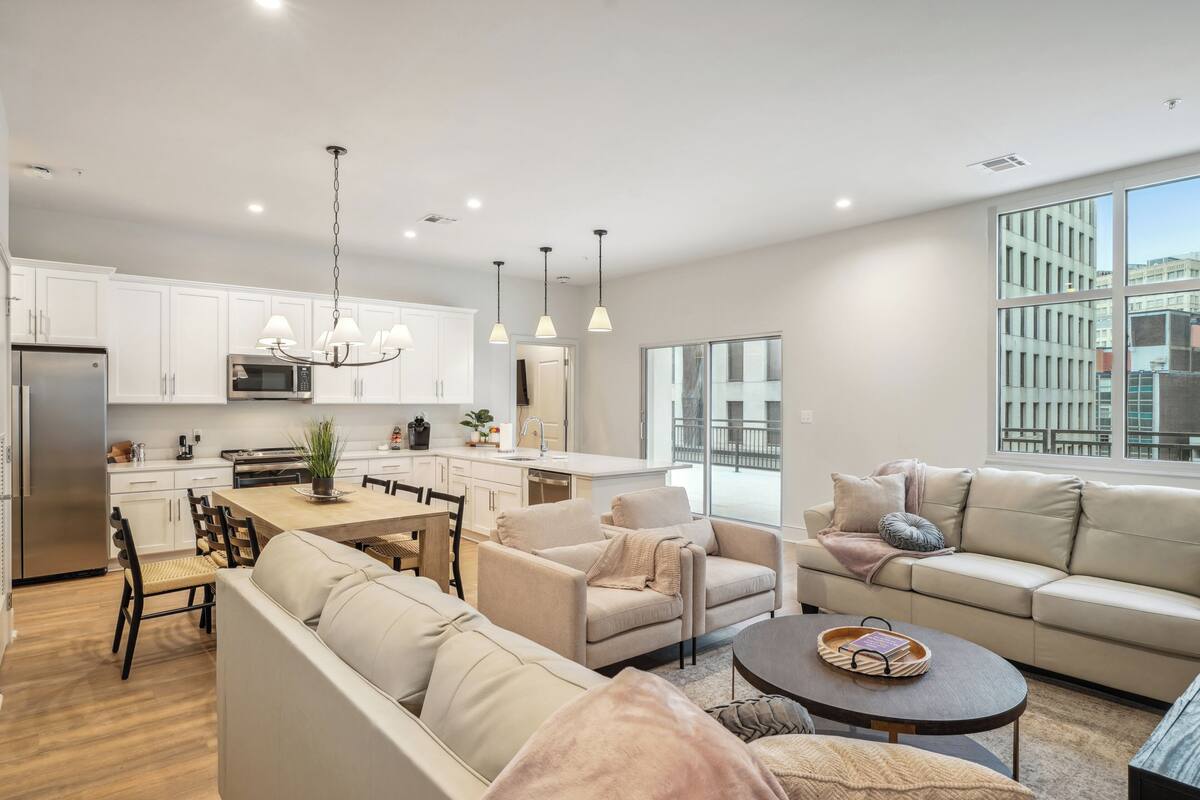 Une cuisine moderne avec des meubles blancs, un coin repas comprenant une table et des chaises, et un salon avec un canapé et une table basse.