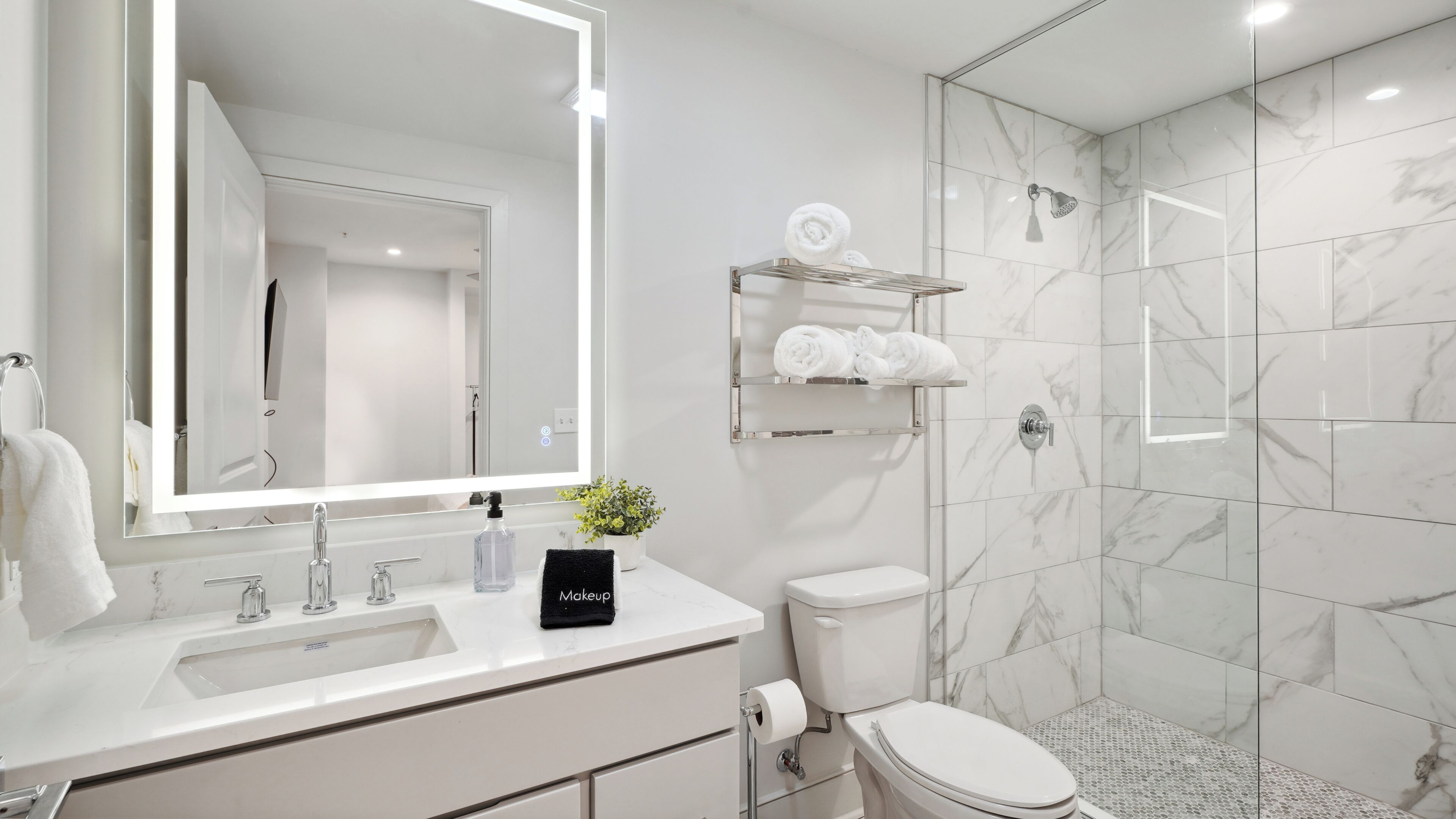 A modern bathroom with a large mirror, white sink, and a glass-enclosed shower.