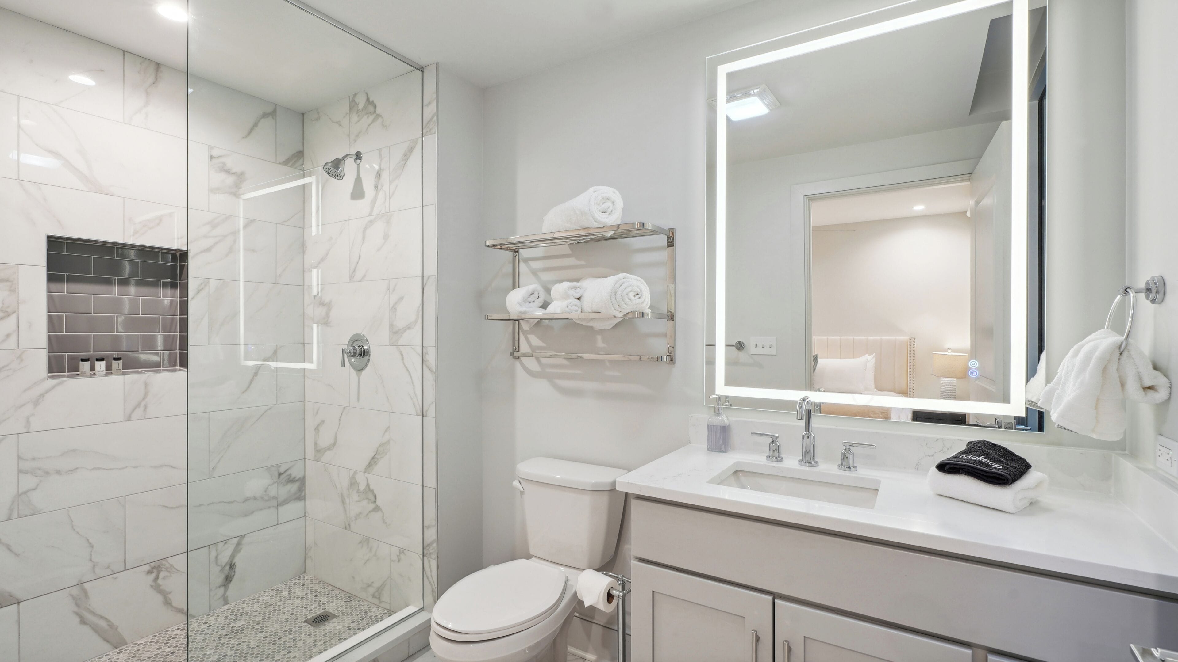 A modern bathroom with a glass-enclosed shower, a toilet, a sink with a mirror, and a towel rack.