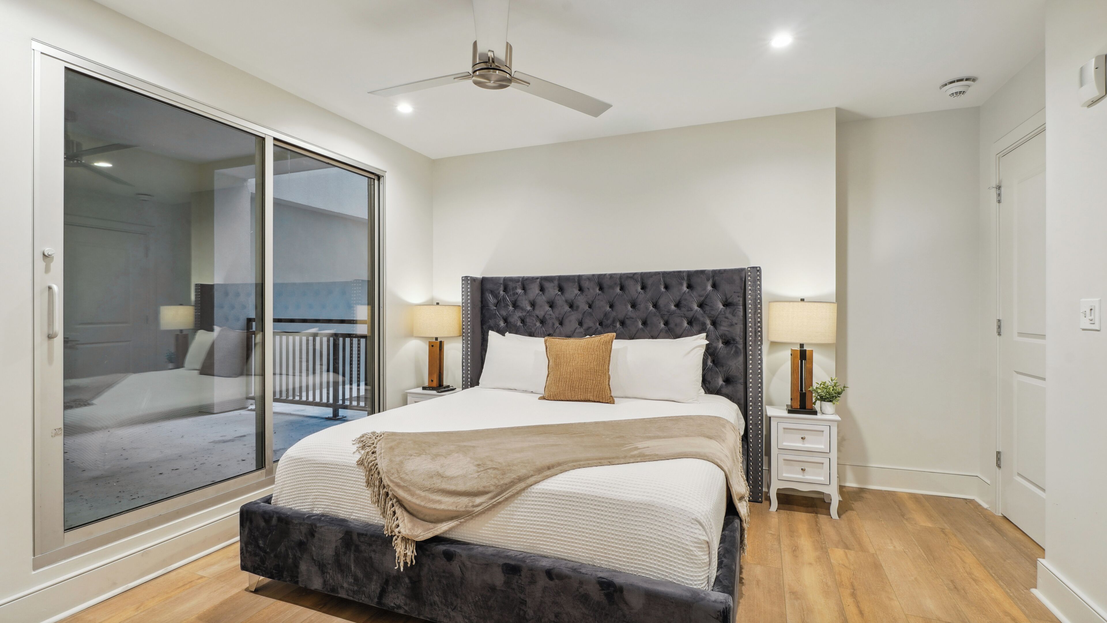 A bedroom with a large bed, a ceiling fan, and a sliding glass door to a balcony.