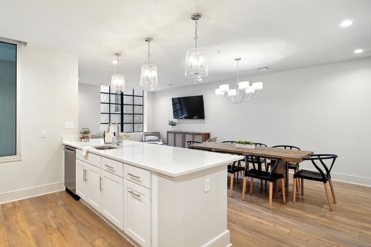 Une cuisine moderne dotée d’un îlot central, de meubles blancs et d’un coin repas avec une table et des chaises en bois.
