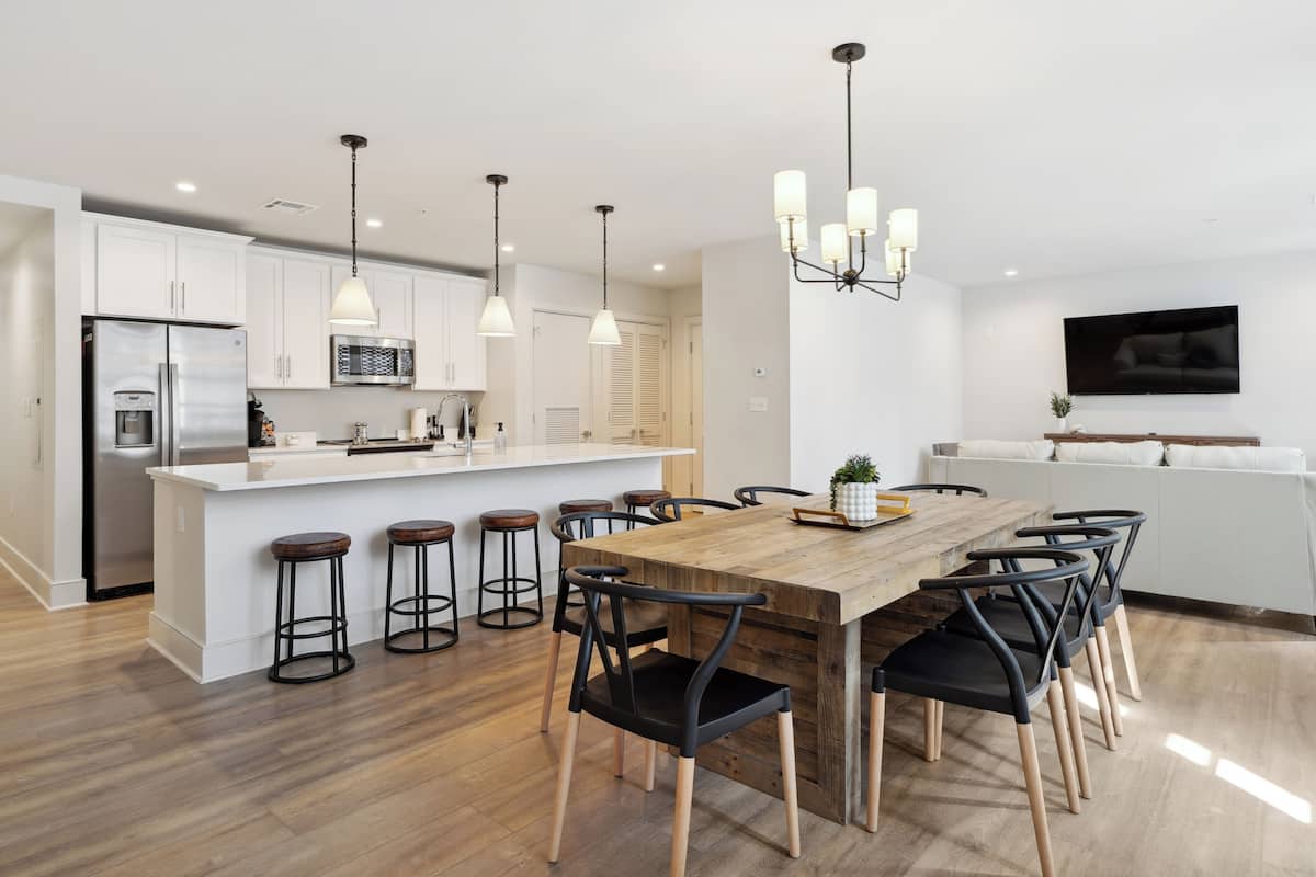 Une cuisine moderne avec des meubles blancs, un réfrigérateur en acier inoxydable et une table à manger en bois, assortie de chaises noires.