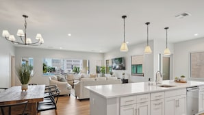 A modern kitchen with white cabinetry, a large island, pendant lighting, and a view of the city through large windows.