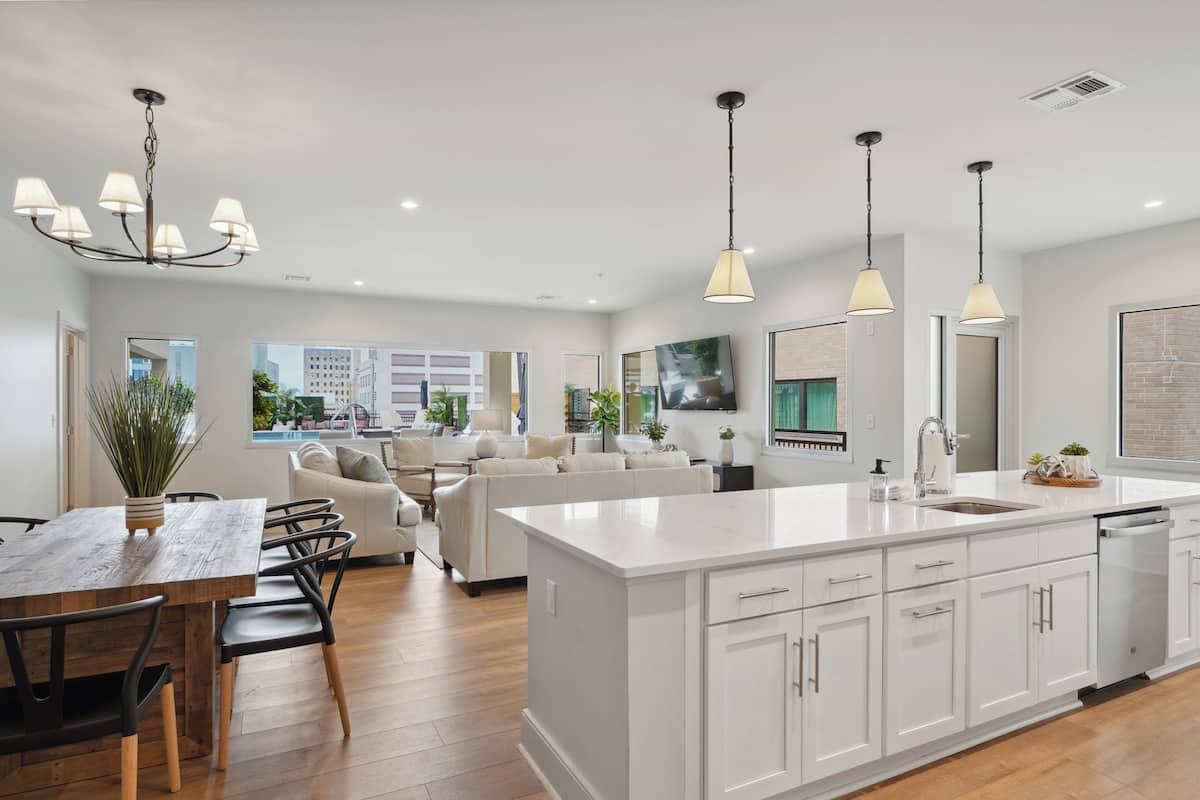 Une cuisine moderne avec des meubles blancs, un grand îlot central, des luminaires suspendus et une vue sur la ville grâce à de grandes fenêtres.