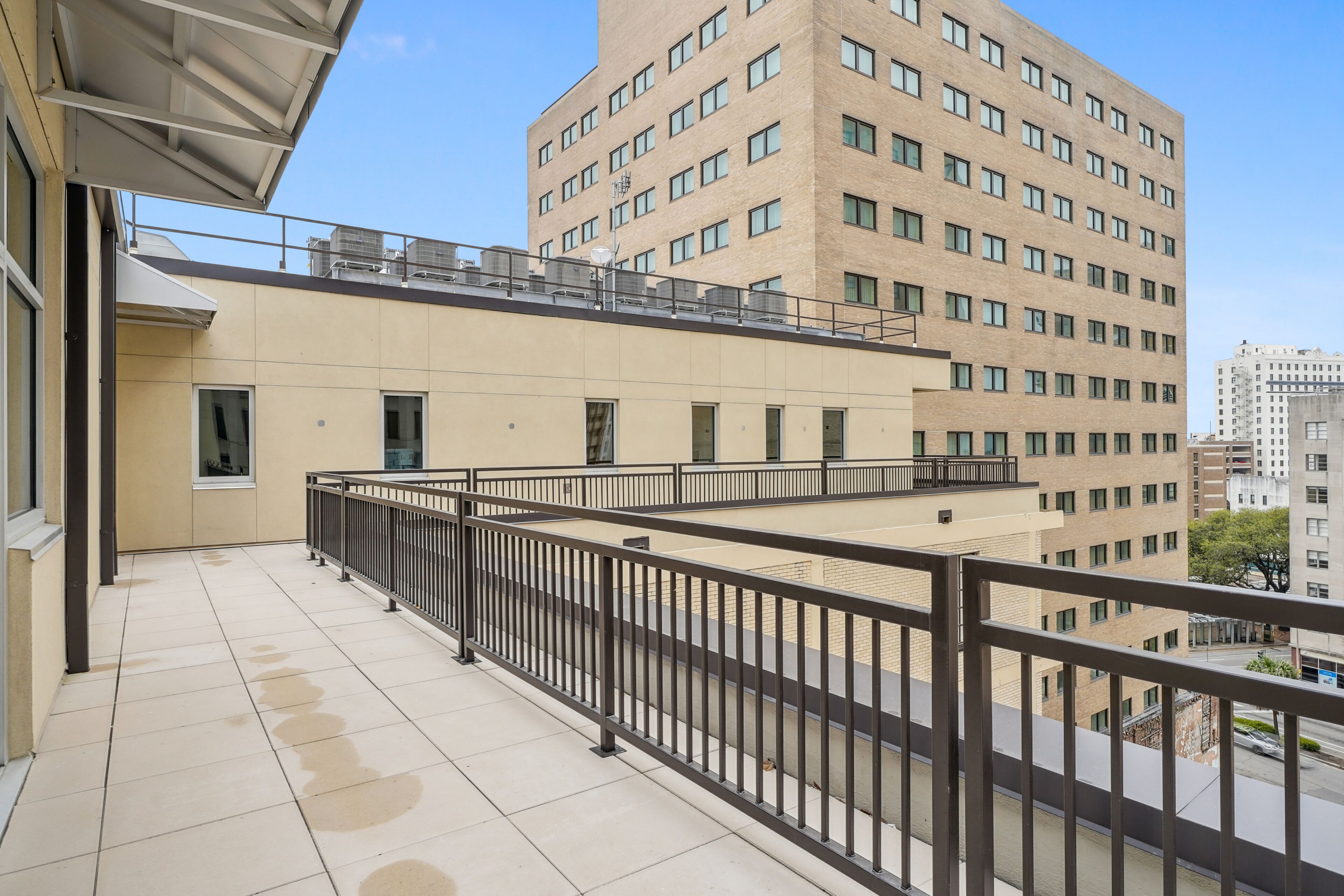 A balcony with a metal railing, a tiled floor, and a view of a multi-story building with numerous windows.