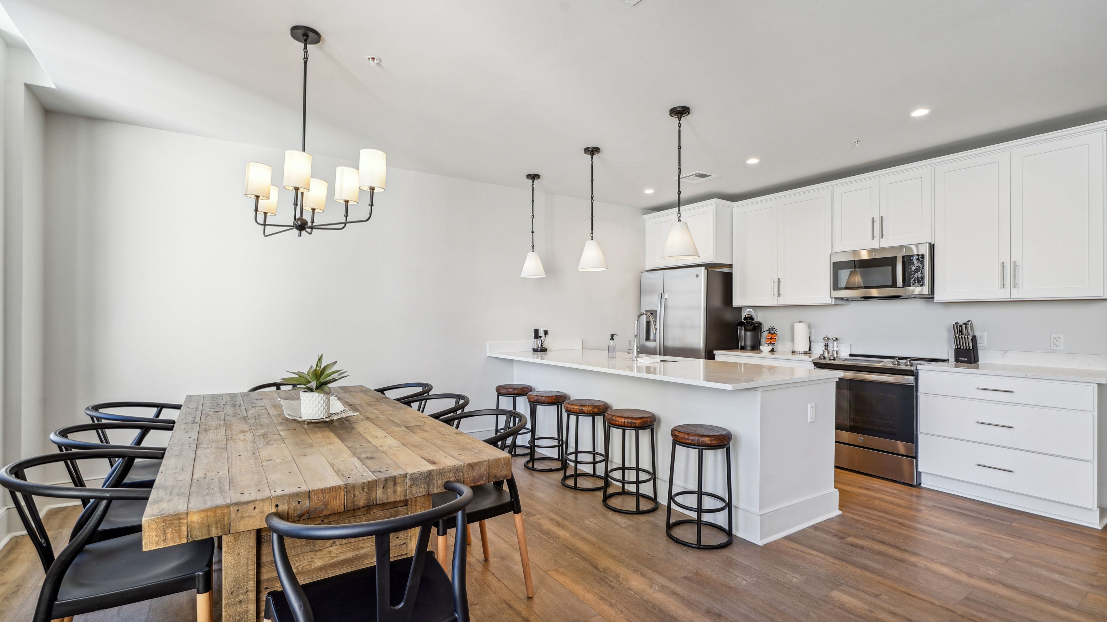 A modern kitchen with white cabinets, stainless steel appliances, and a wooden dining table with bar stools.