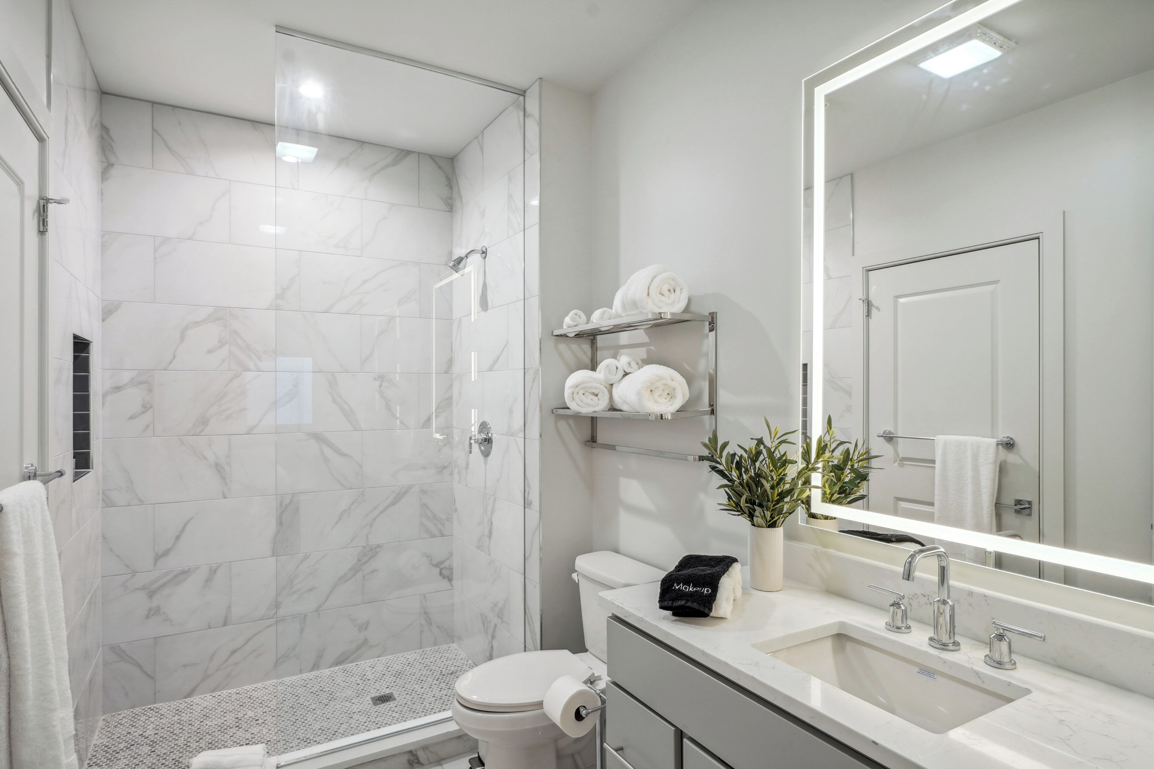 Un baño moderno con ducha de vidrio, inodoro, lavamanos y un espejo grande.