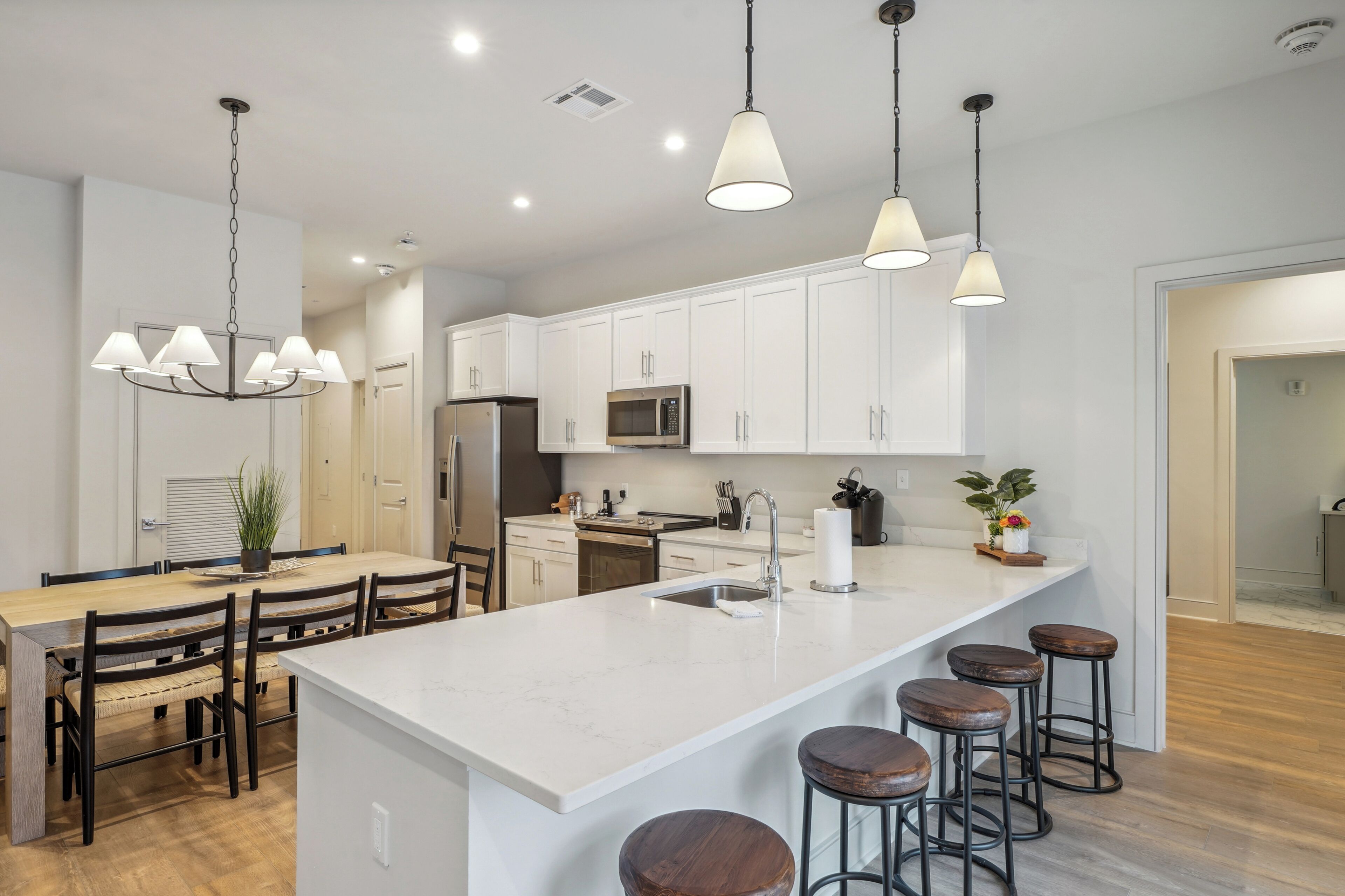 A modern kitchen with white cabinets, a large island with stools, stainless steel appliances, and pendant lighting.