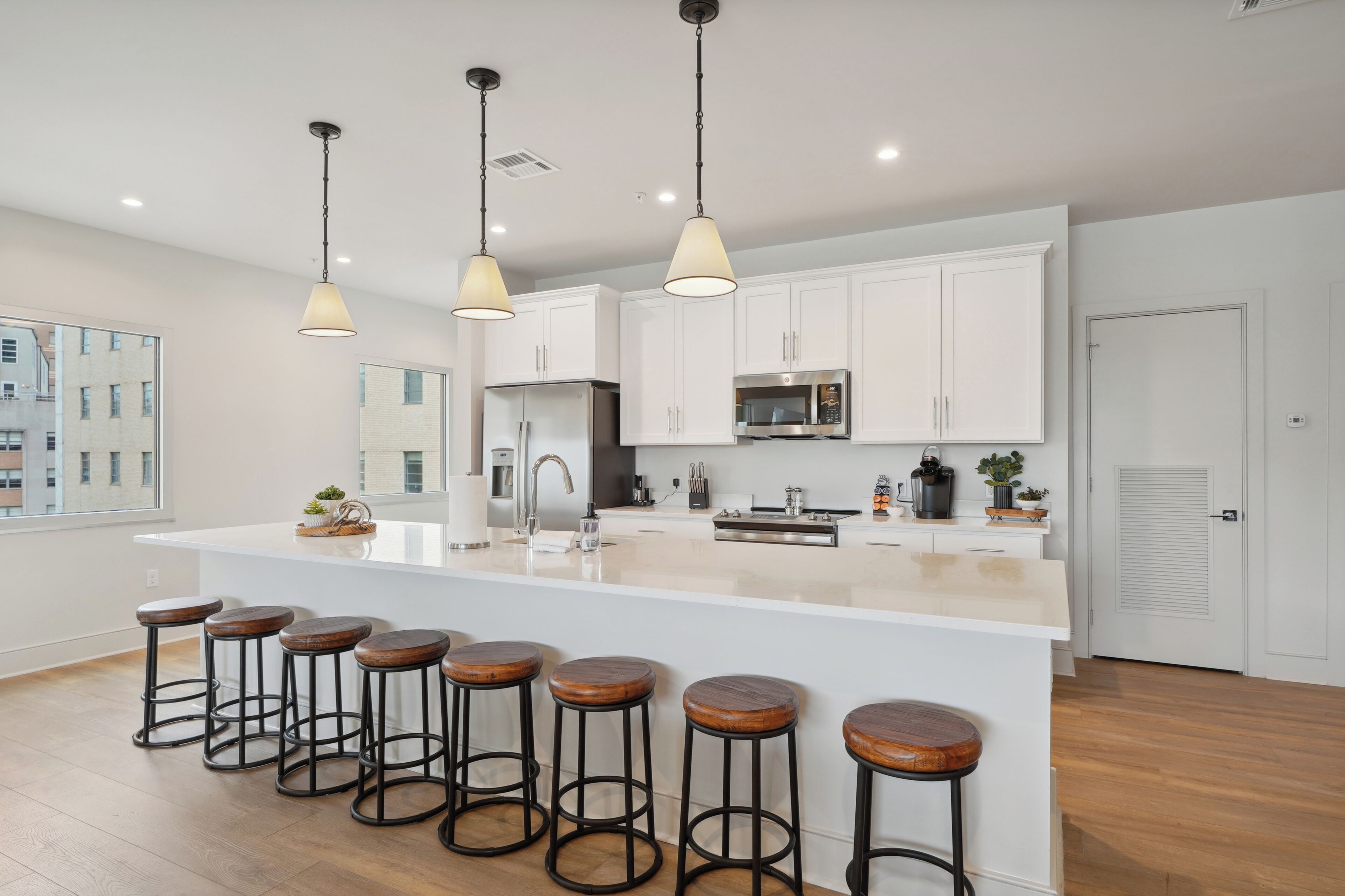 A modern kitchen with white cabinets, a central island with stools, stainless steel appliances, and pendant lighting.