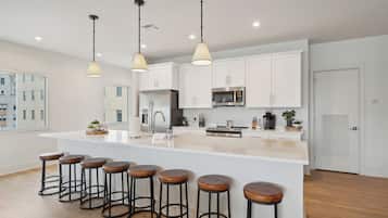 A modern kitchen with white cabinets, a central island with stools, stainless steel appliances, and pendant lighting.