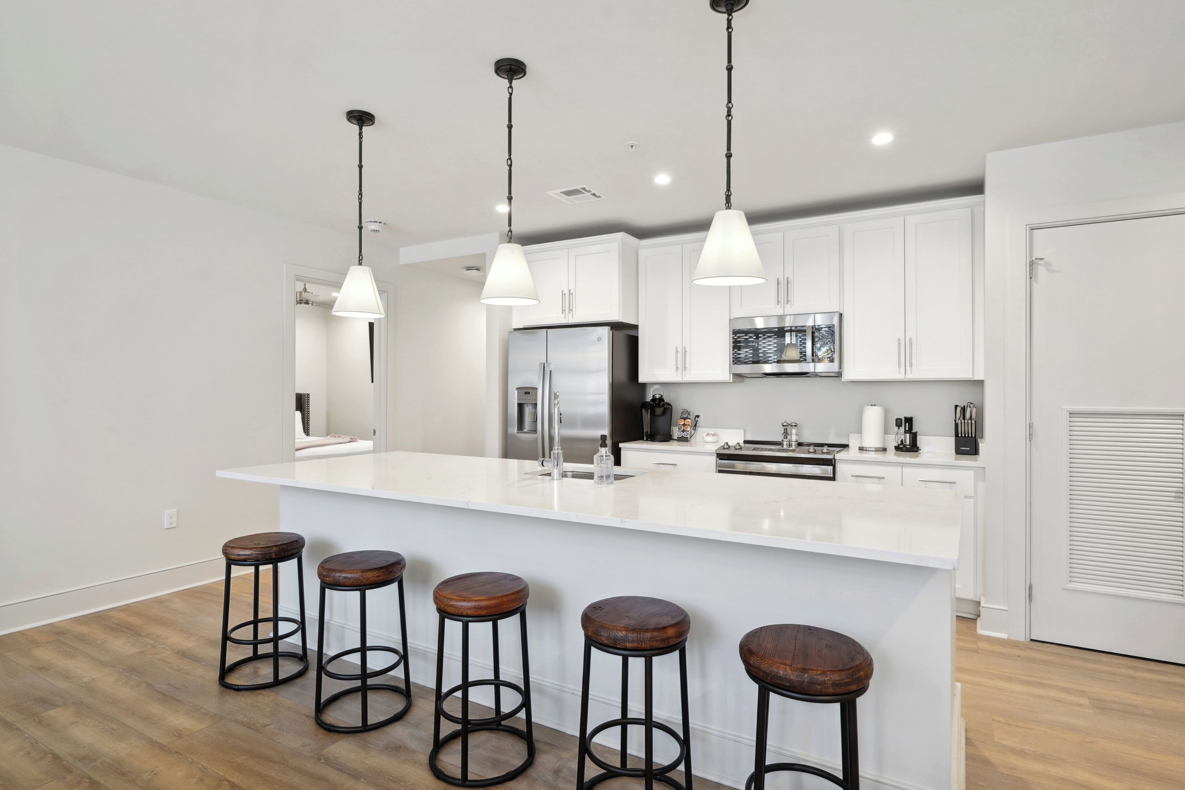 A modern kitchen with white cabinets, a large island with stools, stainless steel appliances, and pendant lighting.