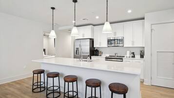 A modern kitchen with white cabinets, a large island with stools, stainless steel appliances, and pendant lighting.