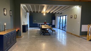 A spacious room with a large dining table, a kitchen area, and a view through glass doors.
