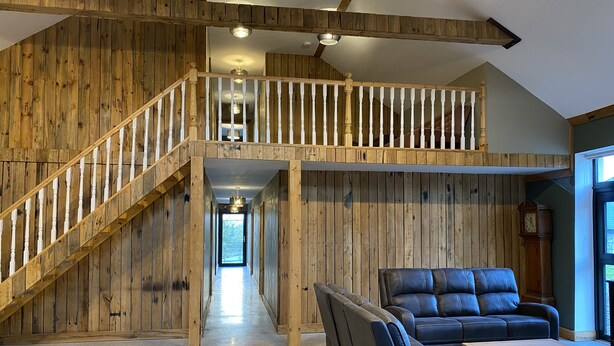 A spacious loft with a wooden interior, a staircase, leather seating, and a view through the open door.
