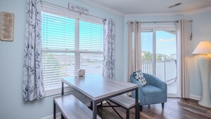 A room with a dining table, a blue armchair, and a view of the outdoors through large windows.