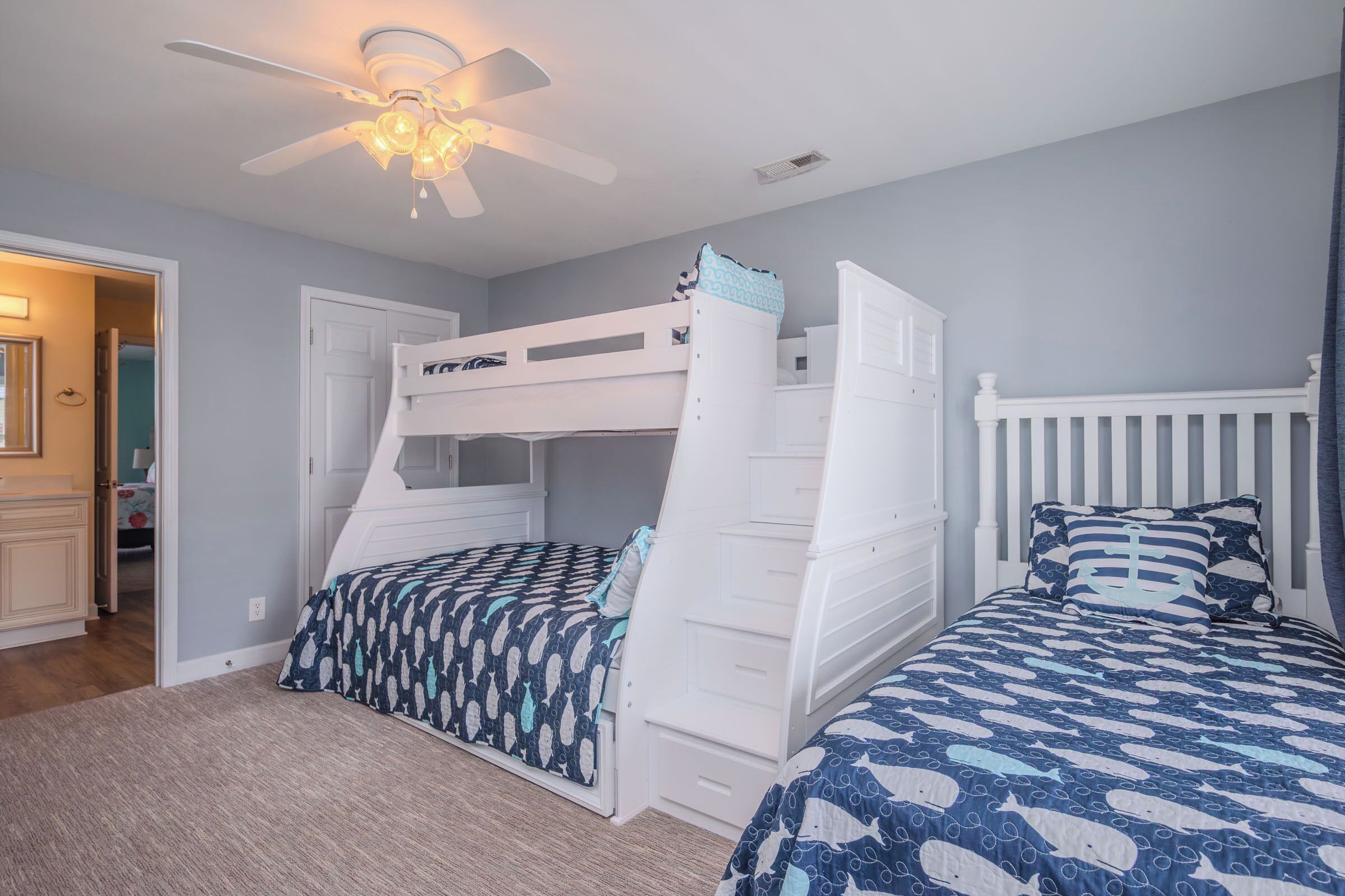A bedroom with bunk beds, a ceiling fan, and a door leading to another room.