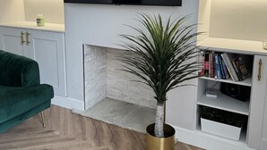 A modern living room with a flat-screen TV mounted on the wall, a green sofa, a fireplace, and a bookshelf with books and decorative items. - Impeccable 3-bed House in Walsall (Walsall)